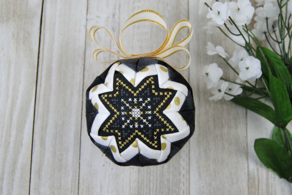 A traditional quilted ornament with a cross stitch center panel.