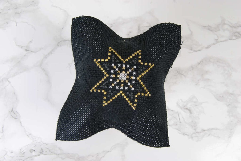 Pin down your cross stitch at the center of the top, bottom, left, and right of your fabric