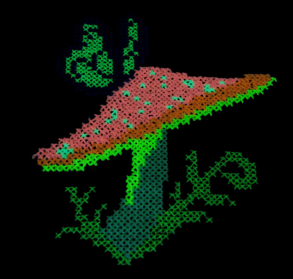 Photo of a glow in the dark cross stitch with the lights off.