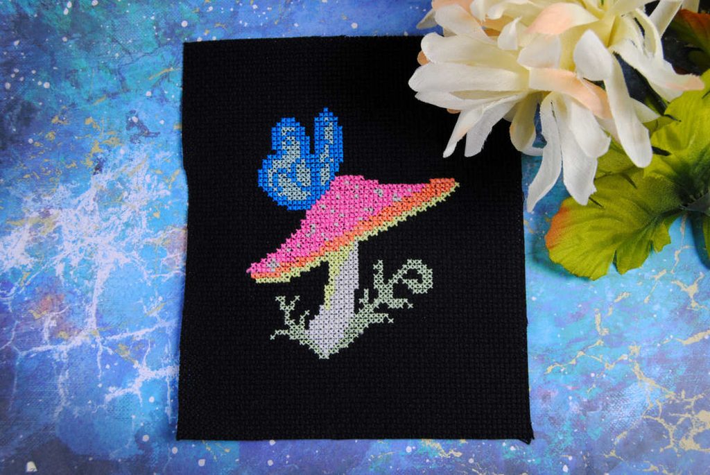 A cross stitch of a mushroom and butterfly in glow in the dark thread.