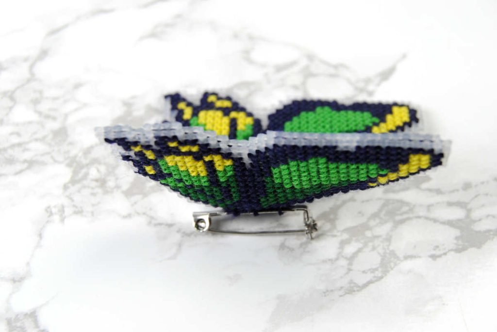 Side view of a cross stitched plastic canvas butterfly pin.