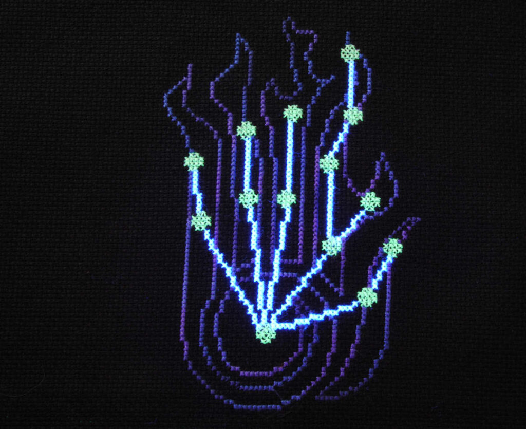 A cross stitch of the Skyrim Destruction skill constellation with the stars in glow in the dark thread under a blacklight.