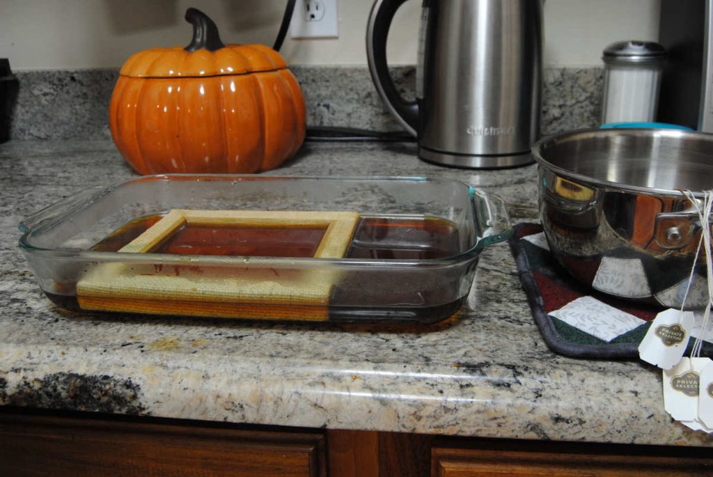 Dyeing / Staining an aida stretched canvas in a glass dish full of black tea.