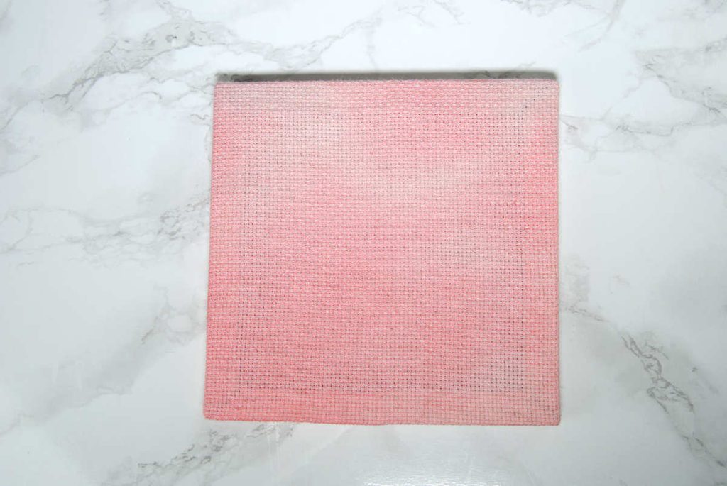 A pre-stretched aida square stained lightly pink using Kool-Aid