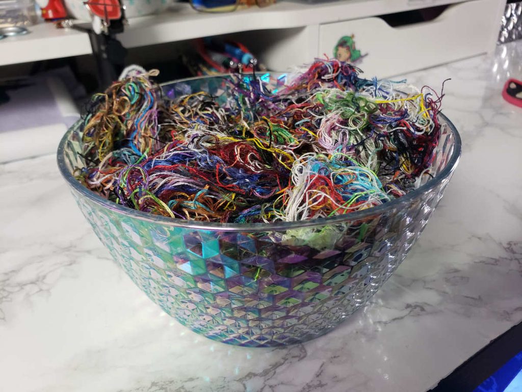 A colorful iridescent bowl full of jumbled thread orts.