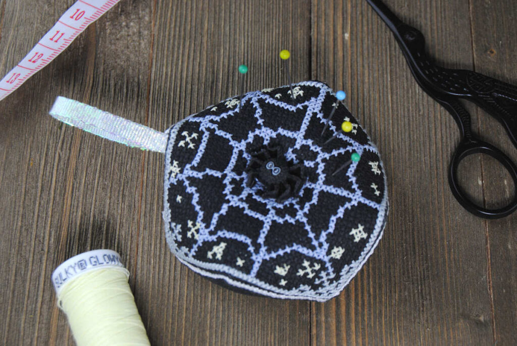 A spiderweb themed biscornu stitched in Sulky Glowy and DMC cotton threads.