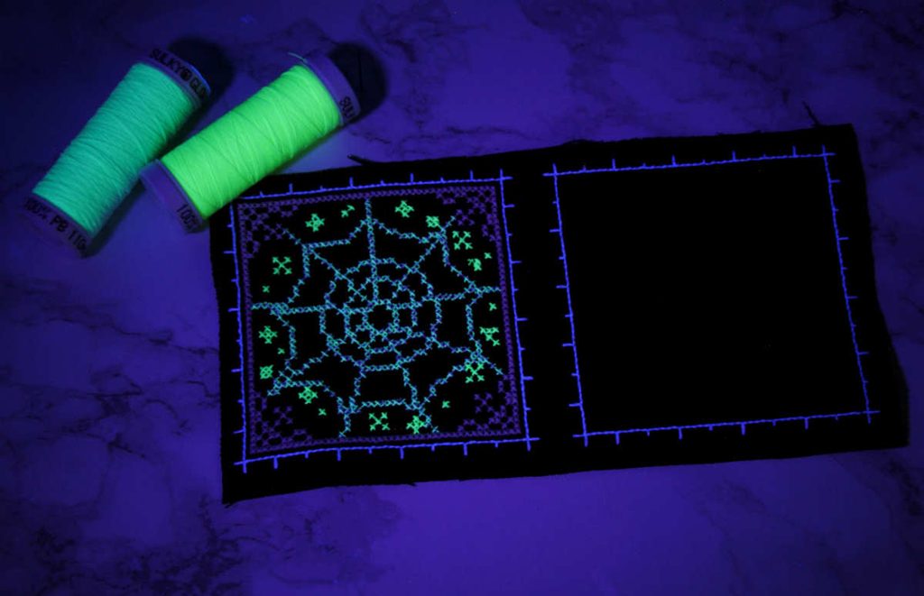 Finished Sulky Glowy spiderweb biscornu design under blacklight