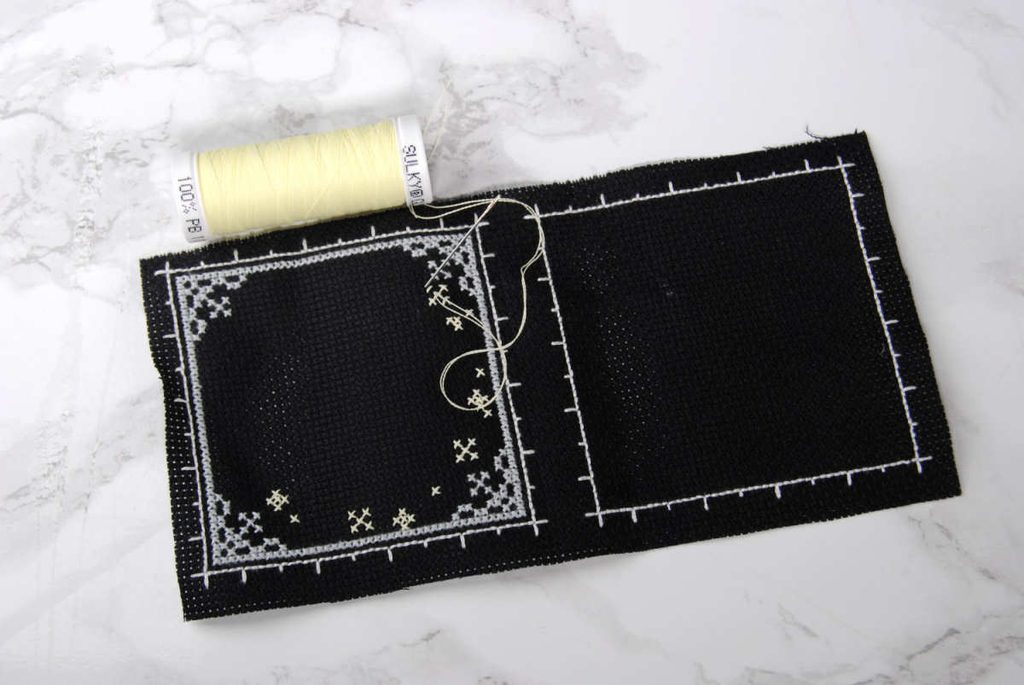 A partially stitched biscornu showcasing coverage of two strands Sulky Glowy on 16 count aida