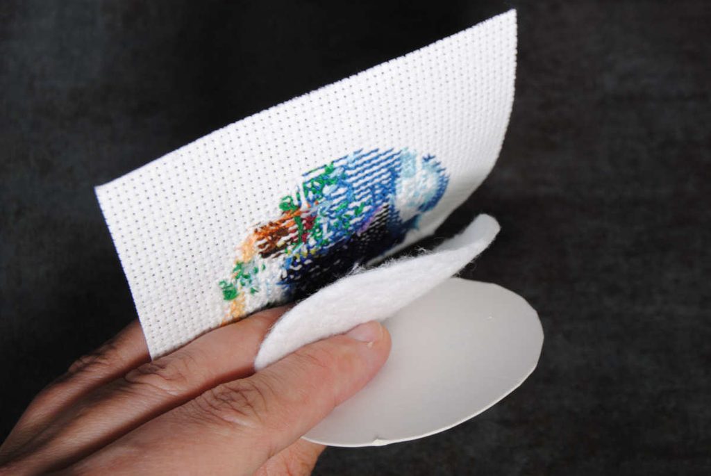 Demonstrating what order to layer cross stitch aida, batting, and cardstock.