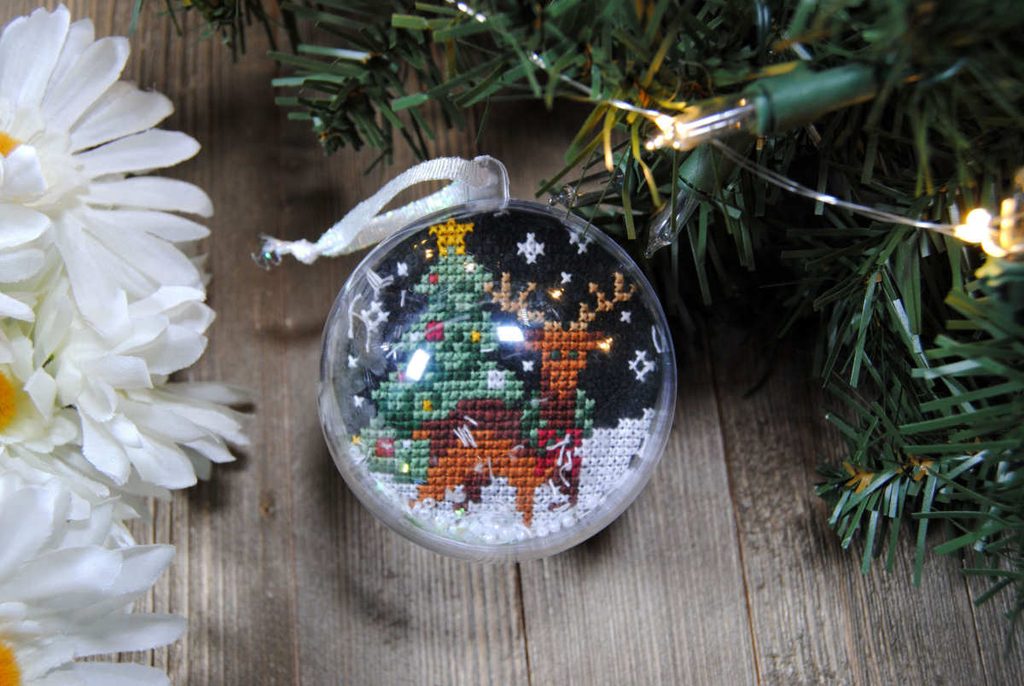 A cross stitched deer in a snowglobe Christmas tree ornament.