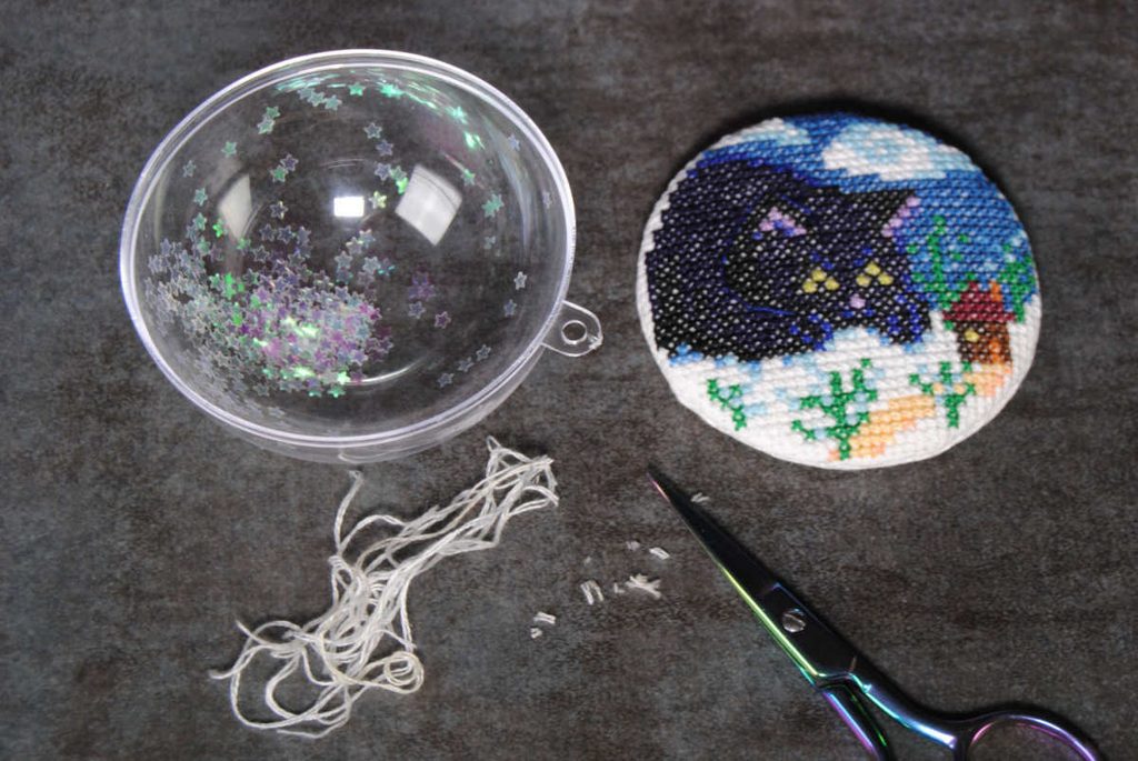 Filling a clear ornament with glitter and thread bits to act as snow.