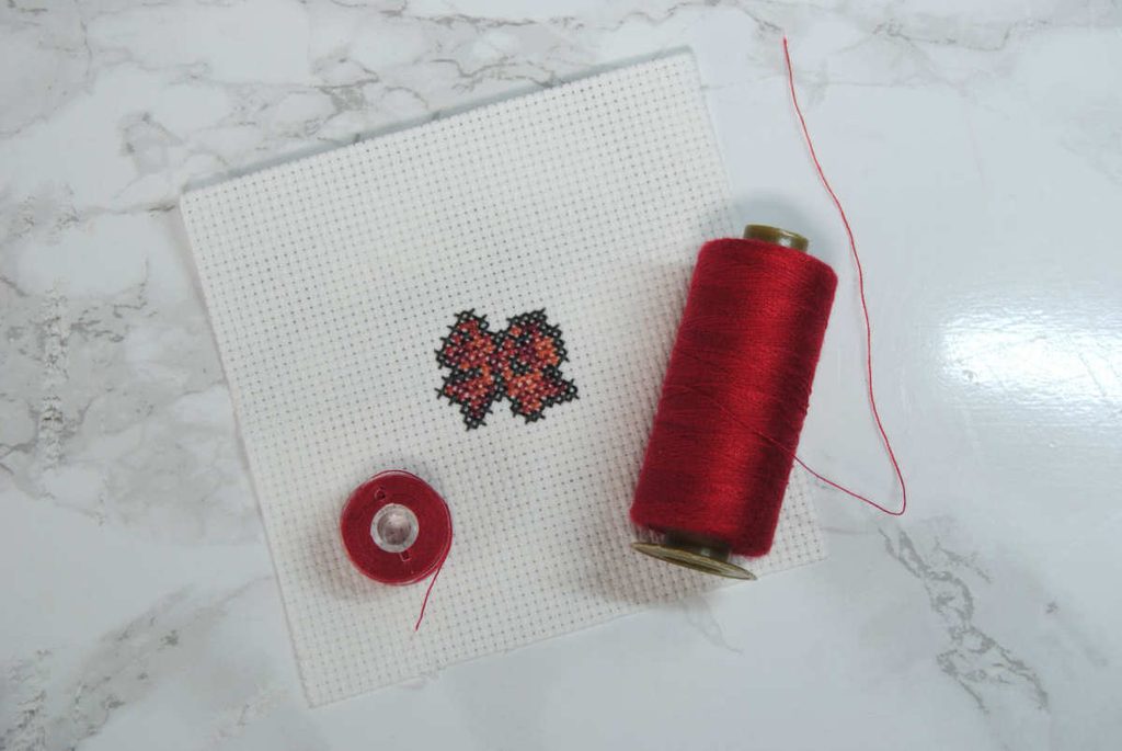 A small cross stitch ribbon with a spool and bobbin of matching colored sewing thread.