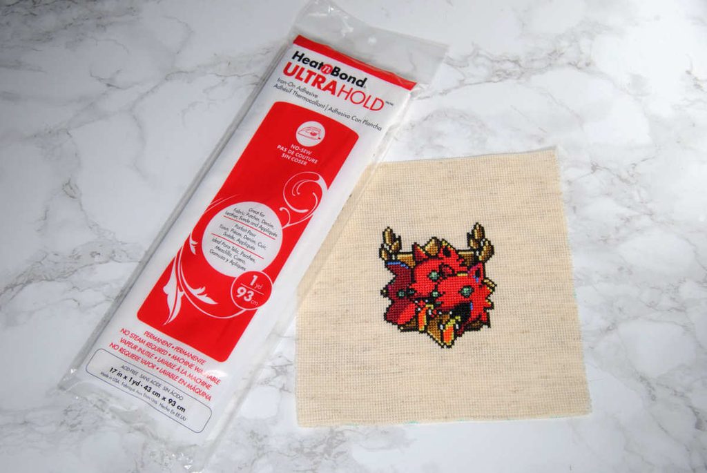 Heat 'n Bond package and a cross stitch of Cerberus from the game Hades