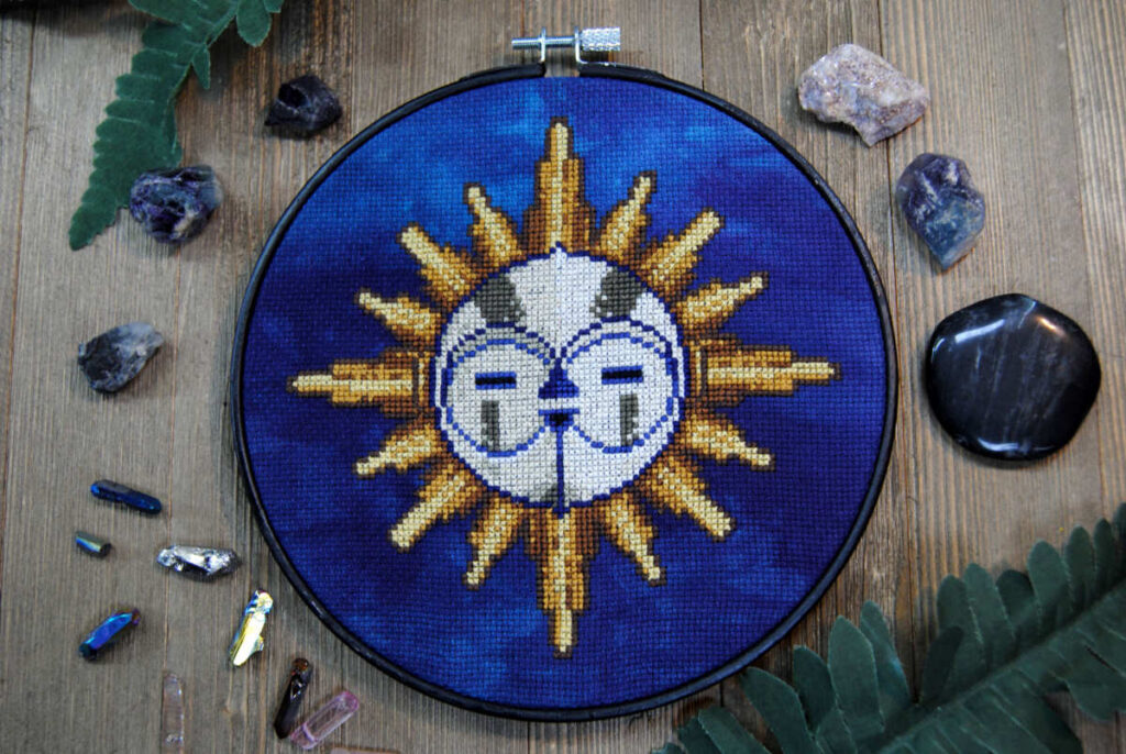 A cross stitch of Esquie from Expedition 33 in a black embroidery hoop.