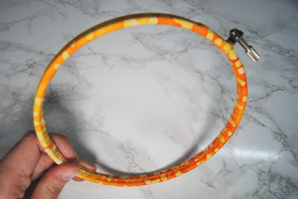 An embroidery hoop wrapped in fabric, tilted so you can see the stitching on the inner hoop.