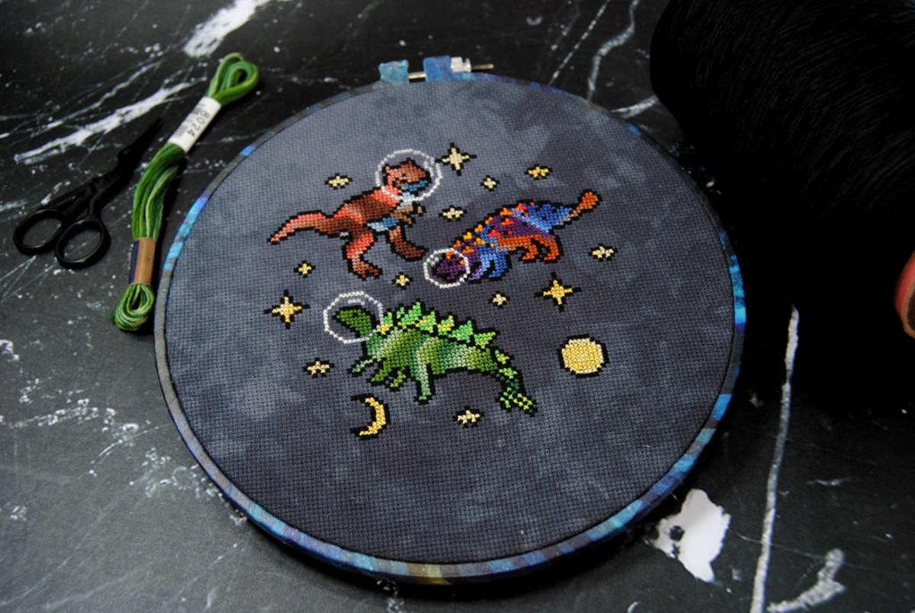 Variegated space dinosaurs cross stitch project in an embroidery hoop.