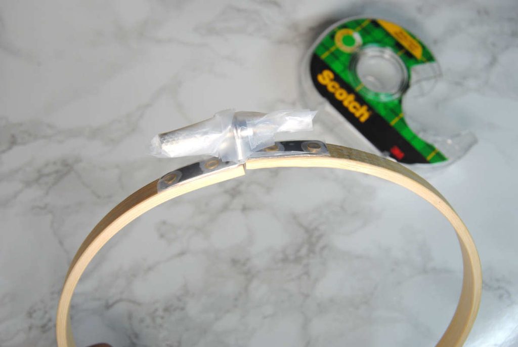 Protecting the metal hardware with clear tape prior to painting an embroidery hoop.