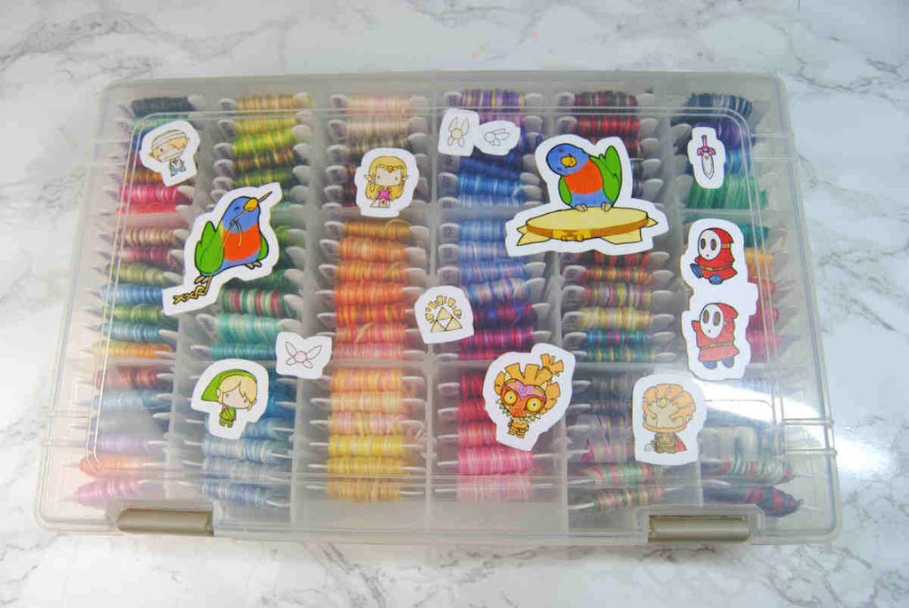A box of embroidery thread bobbins covered in stickers by Zinthings.