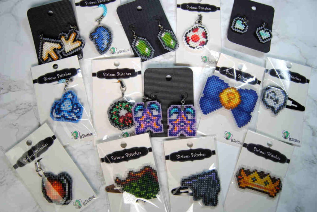 A collection of cross stitched keychains, earrings, and hairclips on plastic canvas.