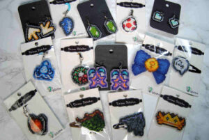 A collection of cross stitched keychains, earrings, and hairclips on plastic canvas.