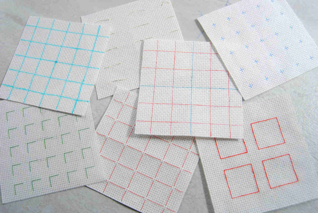 An assortment of small squares of aida showing various different styles of gridding.