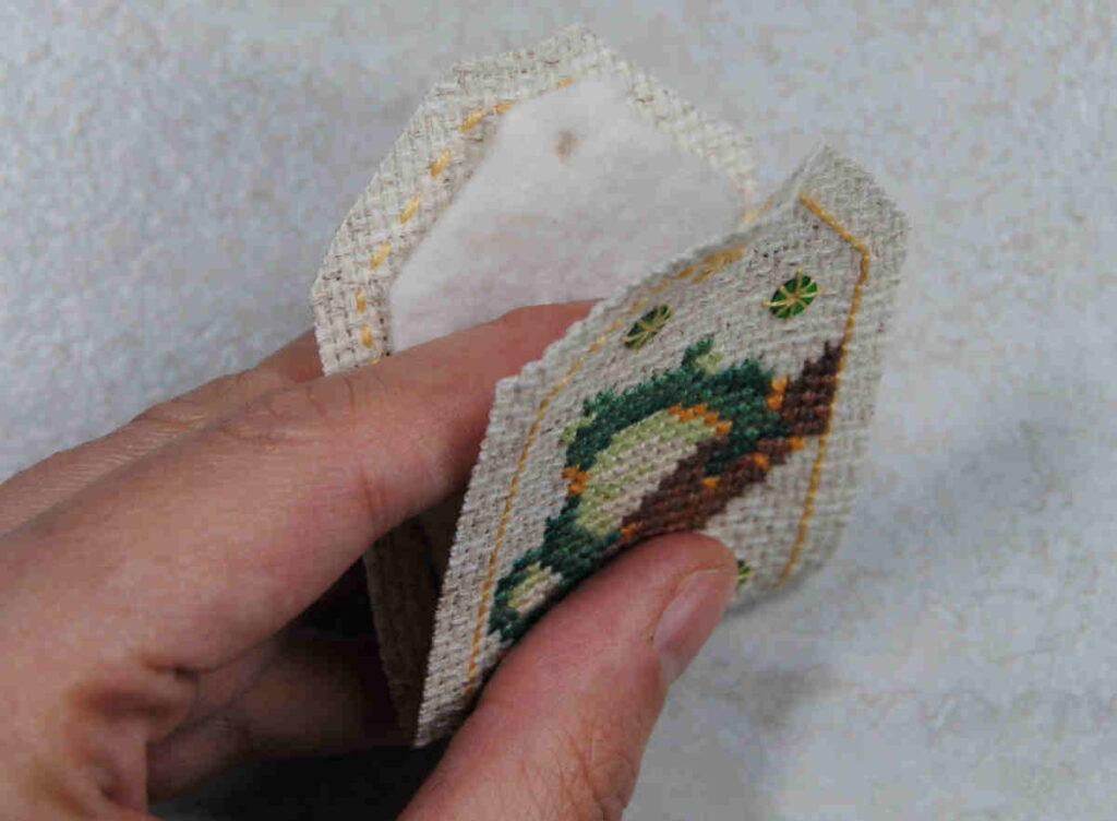 Sizing a piece of batting for your omamori by folding the stitched aida around it.