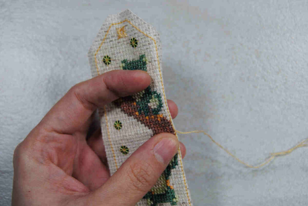 Demonstrating folding the edge of your aida back prior to folding and stitching together.