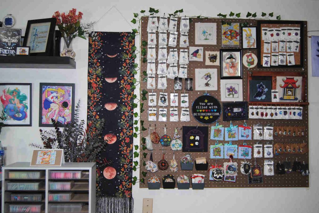 A pegboard in a craft room covered in finished cross stitch pieces.
