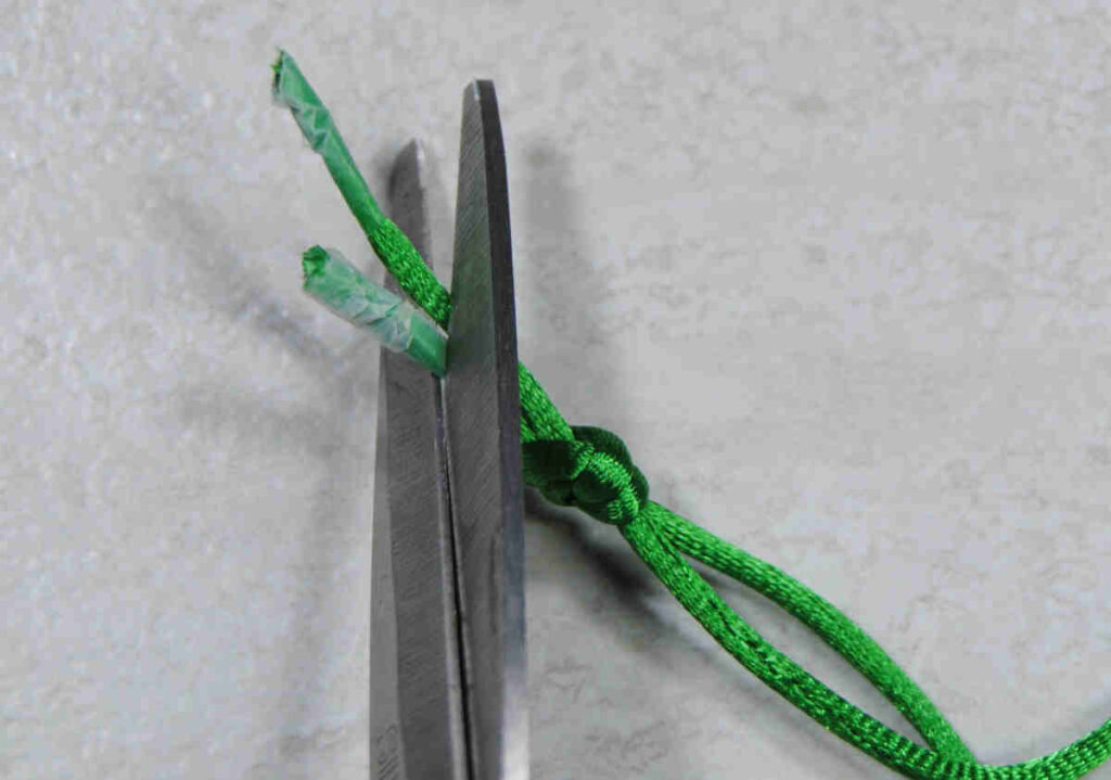 Trimming taped aglets off the end of cording just after the knot.