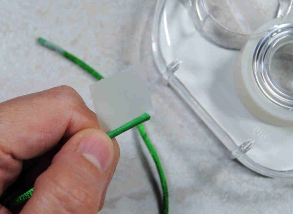 Demonstration of wrapping cord ends with clear tape to create an aglet.