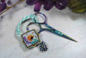 Cross stitch scissor fob featuring beehive and lavender sprig with a beaded tassel