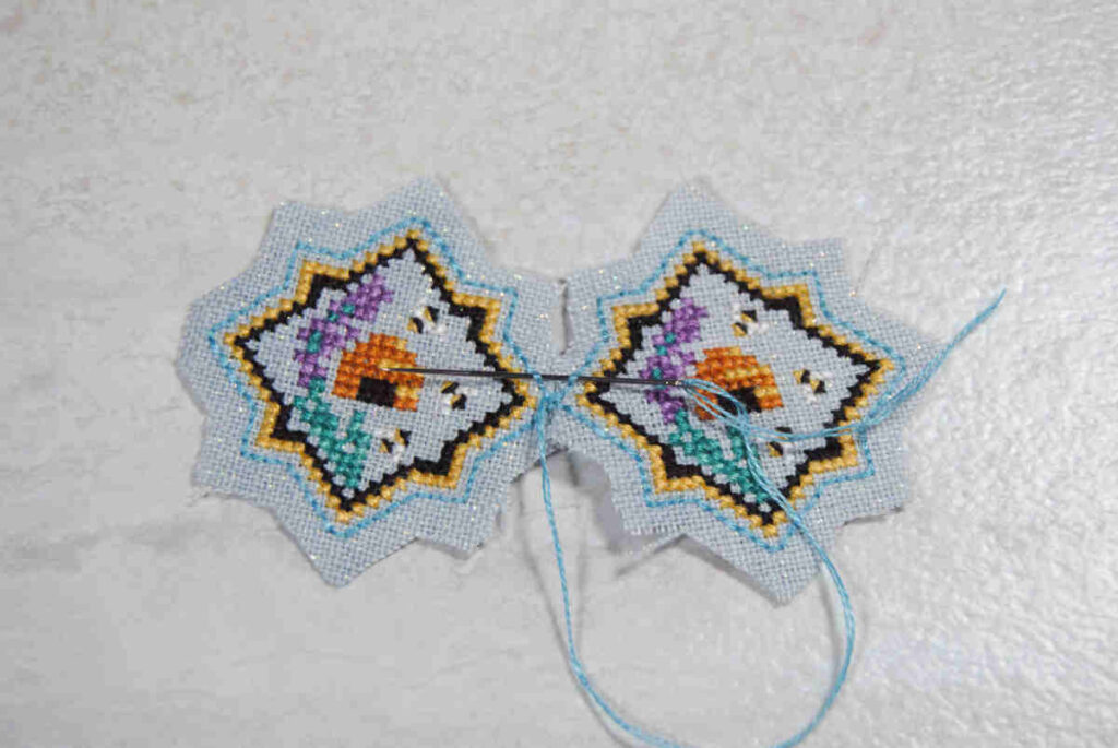 Demonstrating stitching two cross stitches together by sewing under the backstitch outlines.