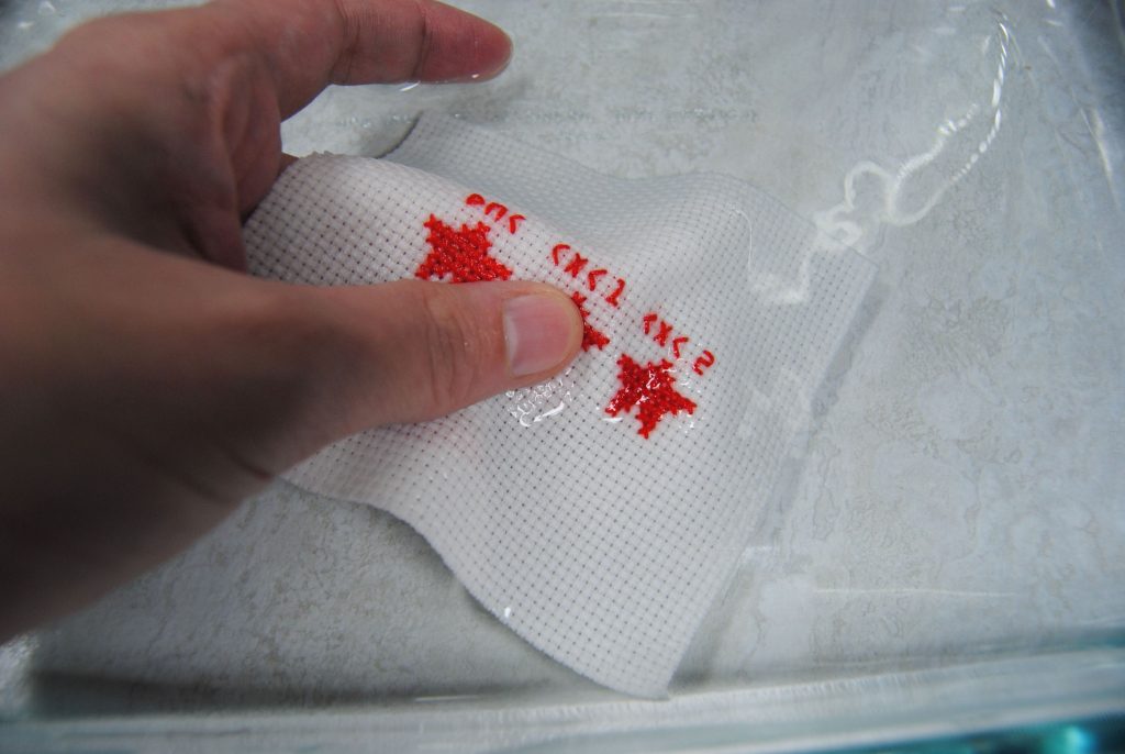 Washing a cross stitch in water to test whether the thread is color fast.