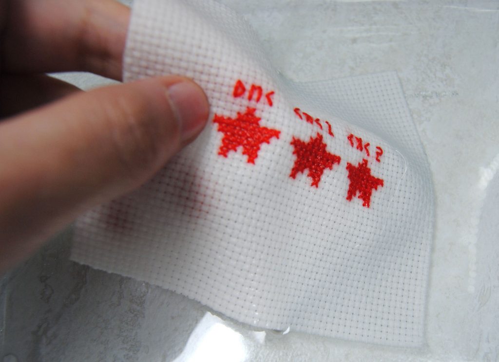 Washing a cross stitch in water to test whether the thread is color fast.