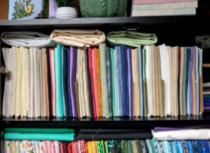 Close up of a fabric cabinet full of cross stitch aida, linen, and evenweave on mini bolts.
